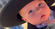 Leignston is registered to the contest to win money with this photo: baby, hat, face, outdoor, sunlight, person, child, carrier, black_hat, curious, portrait, clothing, shadow, daylight, closeup, young_child, expression, casual, background, human