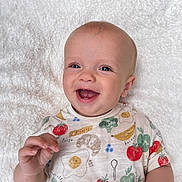 Reuben joined the competition — help win amazing prizes! baby, smiling, infant, child, white_blanket, colorful_shirt, food_print, happy, portrait, cute, young_child, face, hand, lying_down, outdoor, natural_light, skin, head, expression, joy