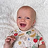 baby, smiling, infant, child, white_blanket, colorful_shirt, food_print, happy, portrait, cute, young_child, face, hand, lying_down, outdoor, natural_light, skin, head, expression, joy