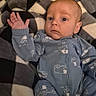 Nolan is registered to the contest to win money with this photo: baby, infant, child, portrait, lying_down, wide_eyes, raised_hand, onesie, blue_clothing, patterned_clothing, blanket, geometric_pattern, bed, indoors, close_up, face, head, cute, calm, photography