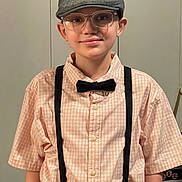 Dustyn is registered to the contest to win money with this photo: child, boy, smile, glasses, hat, cap, bow_tie, suspenders, shirt, portrait, indoor, person, fashion, casual_clothing, young, face, eyewear, standing, childhood, happy