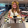 child, cafeteria, lunch, tray, food, carrots, bread, milk, chocolate_milk, golden_crown, costume, toga, smile, person, indoor, table, bench, floor, window, lighting