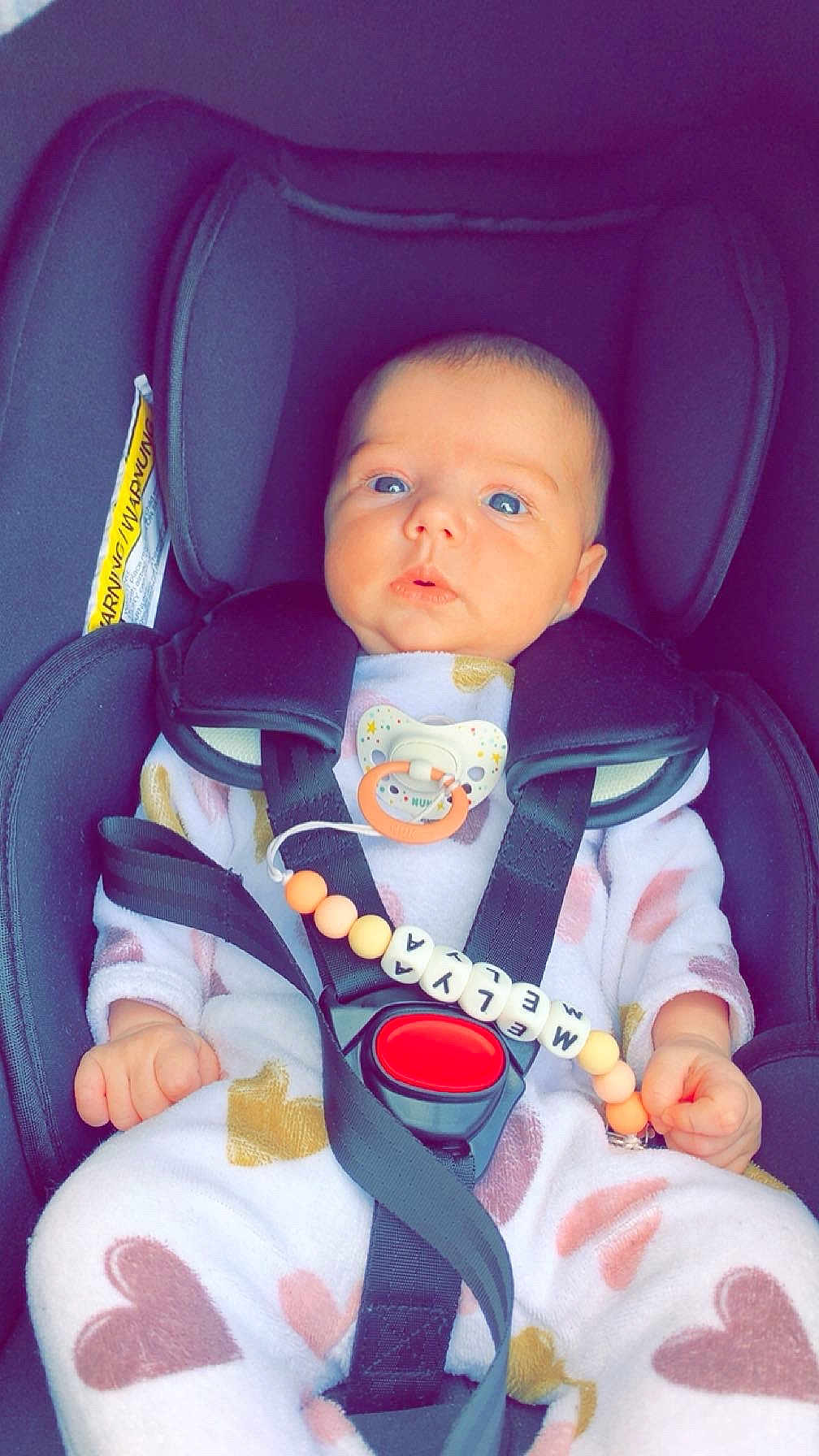 Melya participe au concours pour gagner de l'argent avec cette photo : baby, infant, car_seat, pacifier, onesie, heart_pattern, blue_eyes, seatbelt, child, cute, clothing, toy, indoor, sitting, person, young_child, newborn, straps, safety, closeup