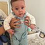 baby, infant, child, overalls, onesie, hands, adult_hand, holding, face, eyes, surprised_expression, blue_clothing, shoes, towel, blanket, changing_table, phone, nursery, portrait, person