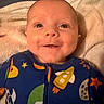 baby, smiling, face, infant, onesie, space_theme, rocket, stars, planet, blanket, close_up, child, cute, happy, indoors, portrait, soft_lighting, young_child, apparel, sleepwear