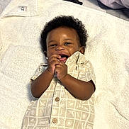 Remy is registered to the contest to win money with this photo: baby, child, smiling, clapping, towel, shirt, patterned_clothing, happy, infant, cute, lying_down, indoor, skin, curly_hair, portrait, small_hands, buttoned_shirt, comfort, soft_texture, light