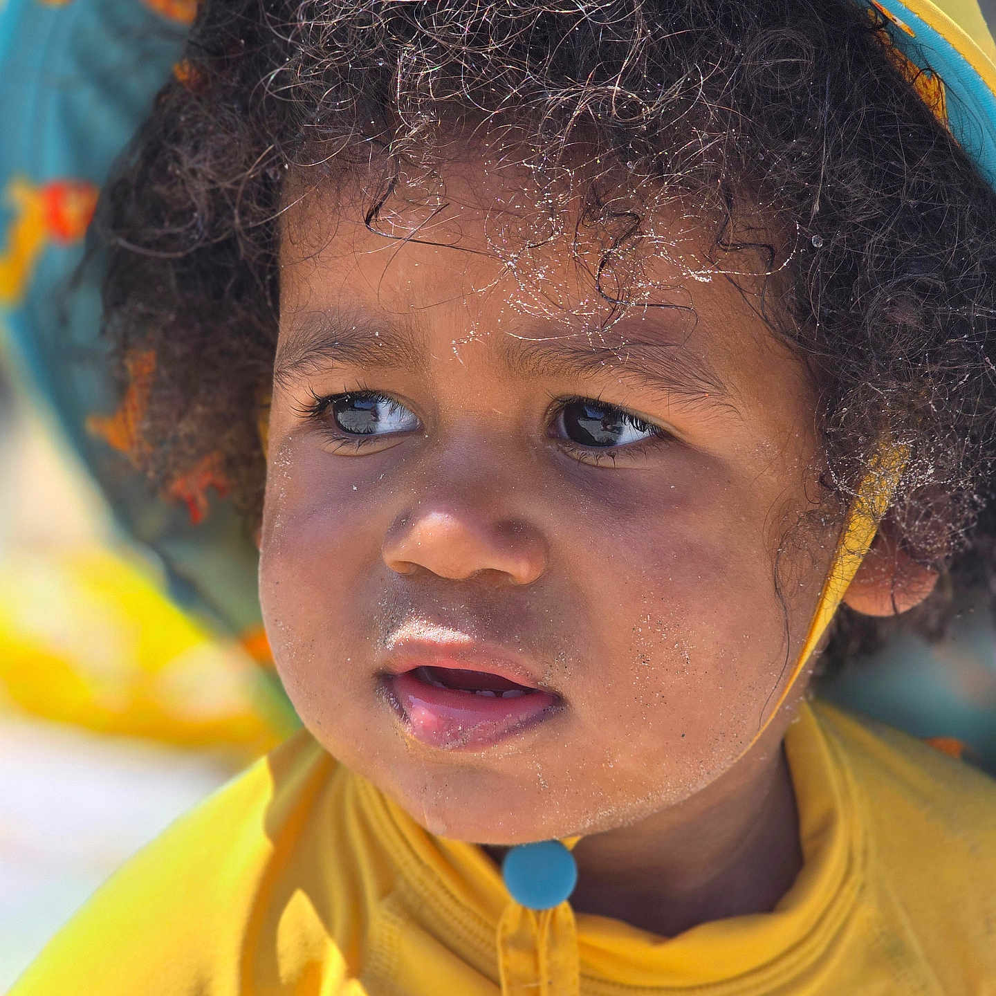 Amadou a rejoint le concours — aidez-le/la à gagner de superbes lots ! casual, child, close_up, curly_hair, cute, daylight, expression, eyes, face, hat, headwear, outdoor, portrait, sand, skin, summer, sunlight, toddler, yellow_clothing, young_child