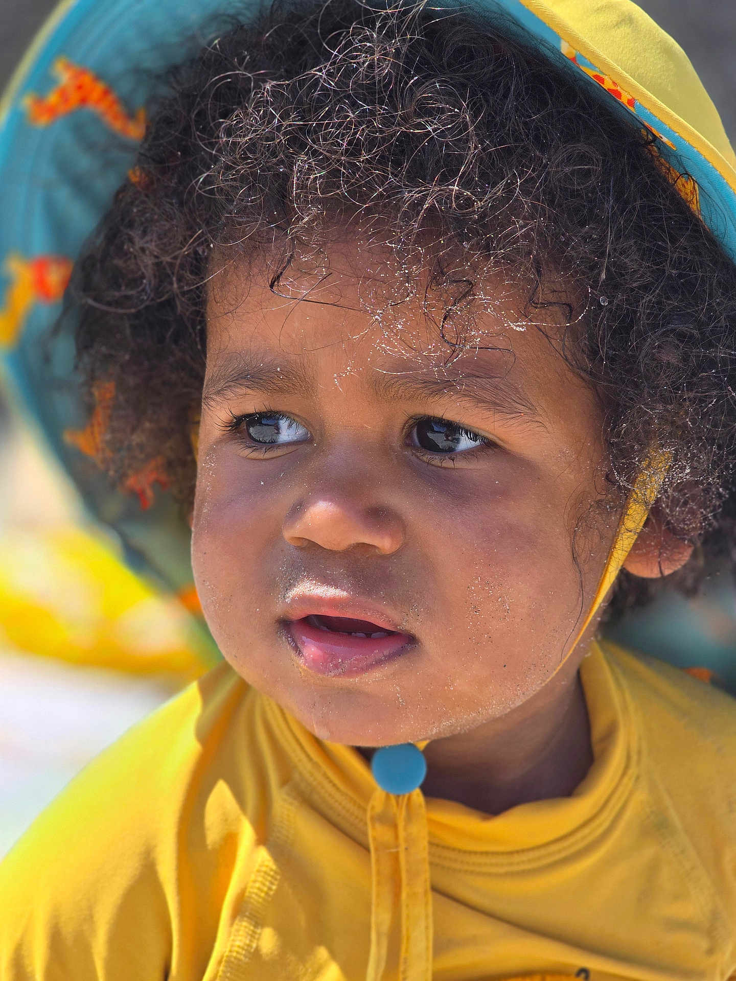 Amadou a rejoint le concours — aidez-le/la à gagner de superbes lots ! child, toddler, face, curly_hair, hat, yellow_clothing, outdoor, sunlight, close_up, portrait, sand, expression, cute, skin, eyes, headwear, summer, daylight, young_child, casual