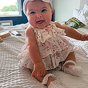 Hallee joined the competition — help win amazing prizes! baby, child, smiling, headband, bow, dress, floral, sitting, bed, white_bedspread, sock, cute, indoors, natural_light, happy, portrait, infant, room, cozy, window