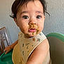 baby_food, bib, chair, child, chubby_cheeks, curious, curly_hair, cute, expression, feeding_time, green_food, high_chair, indoor, looking_up, messy_face, person, skin, table, toddler, young_child