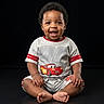 Corey joined the competition — help win amazing prizes! baby, toddler, child, smiling, sitting, clothing, shorts, tshirt, cartoon, race_car, number_95, black_background, studio_photo, barefoot, happy, portrait, cute, indoor, person, infant