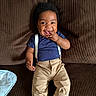Corey is registered to the contest to win money with this photo: baby, child, smiling, happy, couch, brown, clothing, suspenders, pants, shirt, indoor, person, face, cute, infant, sitting, sock, hand, tongue, portrait