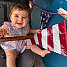 baby, child, smiling, stroller, floral_dress, blue_wall, banner, red_stripes, white_stripes, happy, cute, person, infant, outdoor, hand, foot, face, portrait, seat, colorful