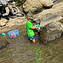 Billie is registered to the contest to win money with this photo: child, boy, water, stream, rocks, green_shirt, camo_hat, plastic_container, toys, nature, outdoors, playing, water_play, summer, reflection, sand, tree, driftwood, shorts, daylight