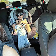 Billie is registered to the contest to win money with this photo: toddler, child, car_seat, sunglasses, clapping, car_interior, family, smiling, seatbelt, blanket, toy, adult, window, sunlight, headrest, backseat, person, casual_clothing, happy, travel
