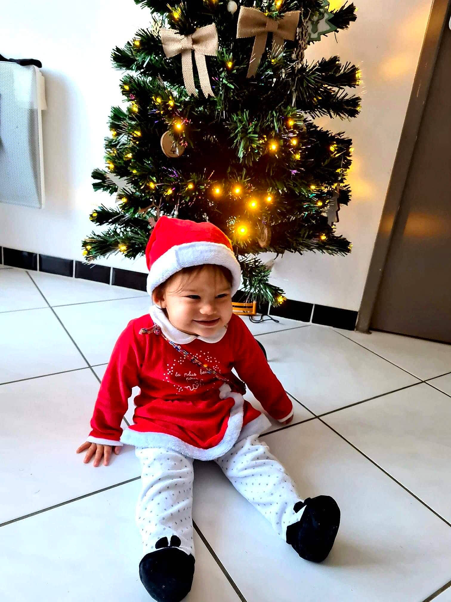 Lou-maï participe au concours pour gagner de l'argent avec cette photo : baby, baby_toddler_clothing, carmine, child, christmas, christmas_decoration, christmas_eve, christmas_lights, christmas_ornament, christmas_tree, costume_accessory, floor, flooring, headwear, holiday, holiday_ornament, human_body, interior_design, joy, ornament