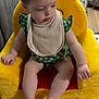 Brynlee is registered to the contest to win money with this photo: baby, child, green_clothing, bib, plush_chair, yellow_chair, indoor, face, person, sitting, floor_mat, toy_chair, home, furniture, wood_floor, short_hair, cute, infant, legs, arm