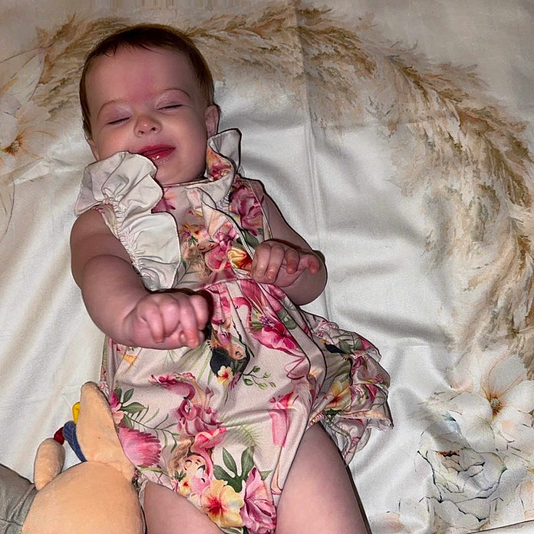 Brynlee is registered to the contest to win money with this photo: baby, baby_clothing, blanket, child, closed_eyes, cute, fabric, floral_dress, flower_pattern, happy, home, infancy, infant, lying_down, numbers, person, plush_toy, portrait, smiling, soft_toy