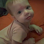 Brynlee is registered to the contest to win money with this photo: baby, infant, child, face, eyes, smile, pink_clothing, skin, hand, arm, lying_down, indoor, bed, orange_bedspread, tattoo, person, cute, young, portrait, looking_up