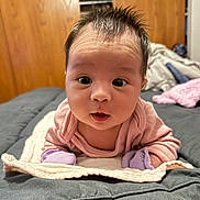 Lexi is registered to the contest to win money with this photo: baby, bed, blanket, child, closeup, cozy, curious_expression, cute, indoor, infant, mittens, person, pink_clothing, portrait, purple_mittens, soft_lighting, spiky_hair, tummy_time, wide_eyes, wooden_wall