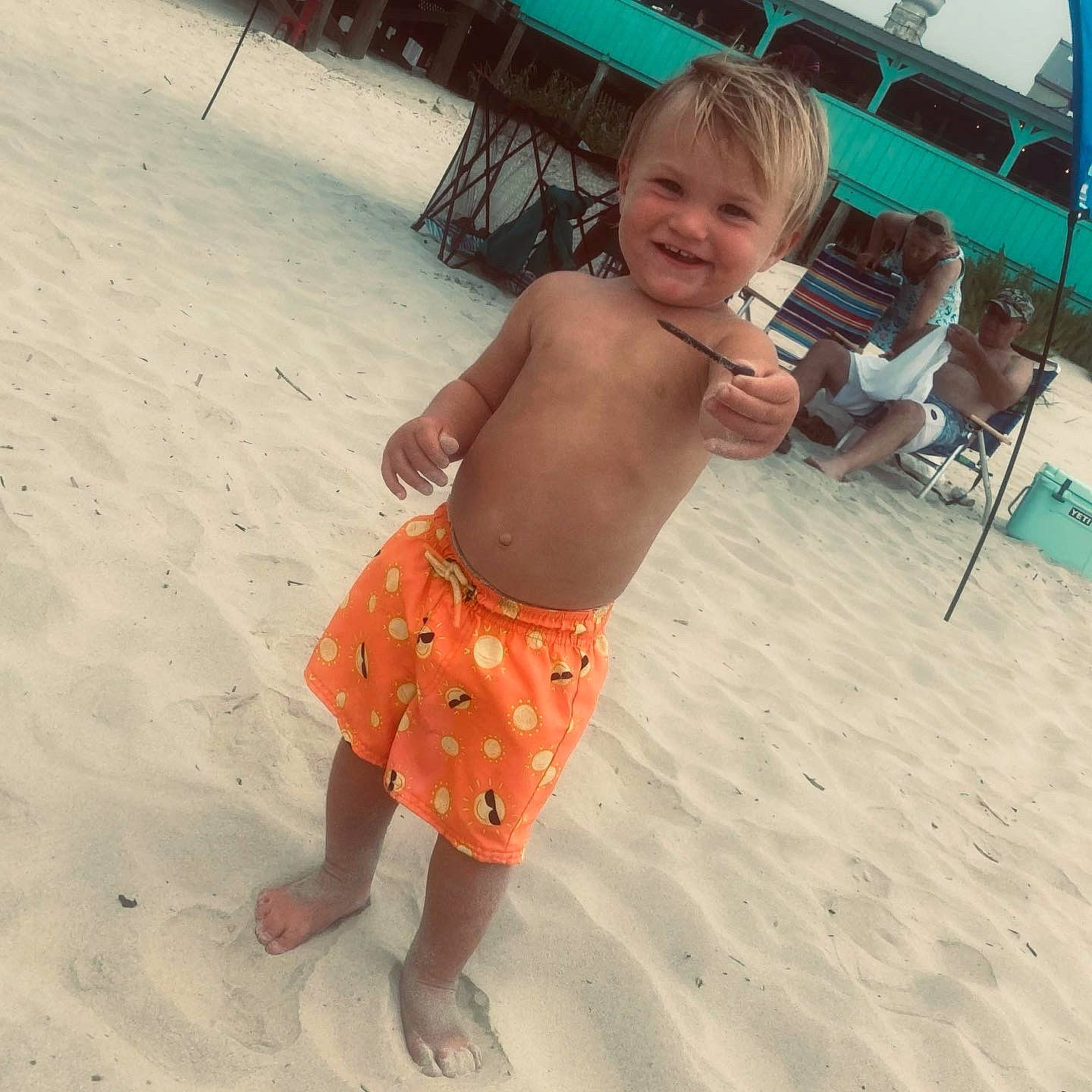 Memphis is registered to the contest to win money with this photo: barefoot, beach, board_short, chair, chest, foot, fun, hair, happy, head, human_leg, joy, leisure, people_on_beach, person, sand, sleeve, smile, toddler, trunk