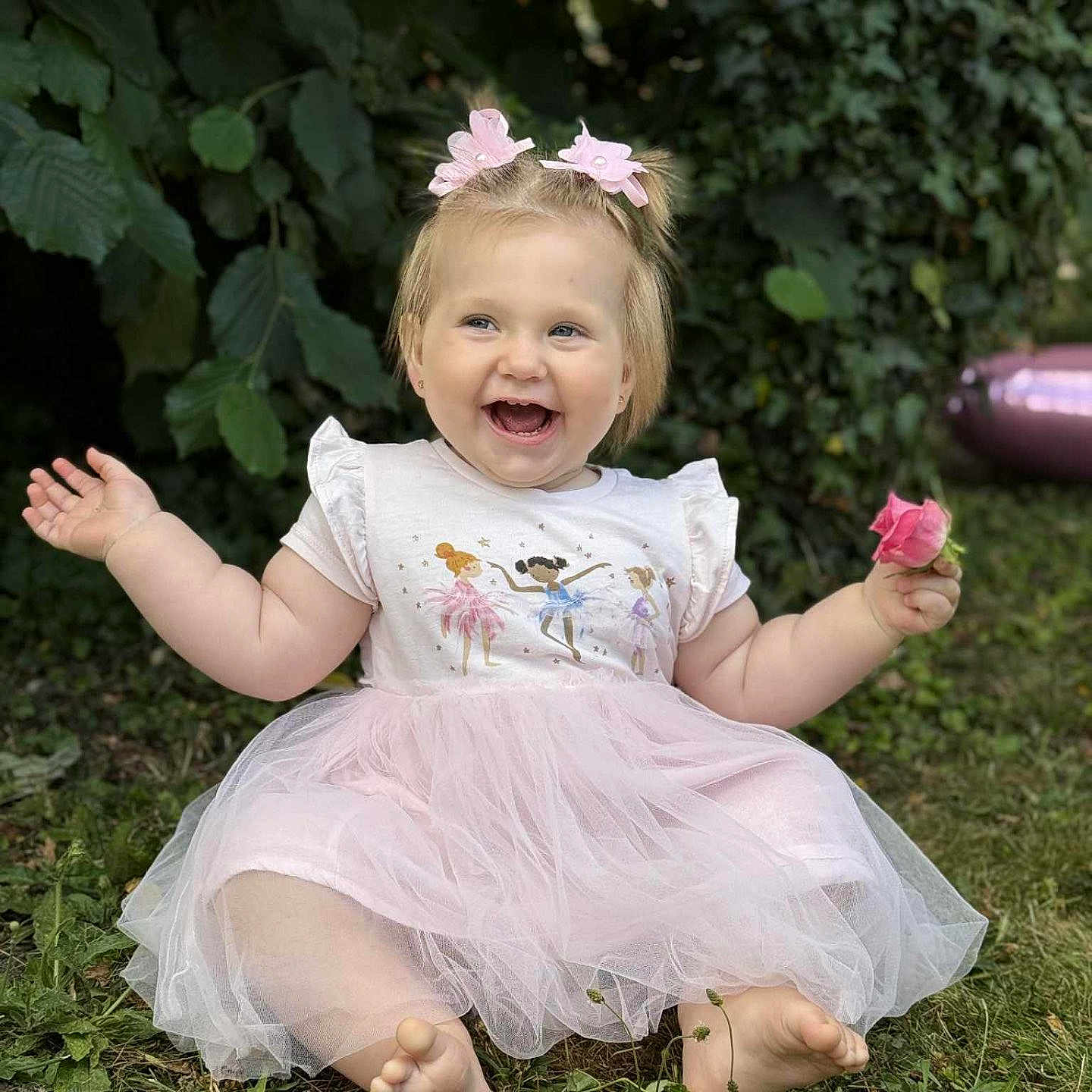Arina a rejoint le concours — aidez-le/la à gagner de superbes lots ! barefoot, child, cute, daylight, flower, fun, grass, greenery, hair_bows, happy, nature, outdoor, petals, pink_dress, playful, portrait, sitting, smiling, toddler, young_child
