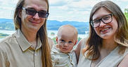 Asher is registered to the contest to win money with this photo: family, baby, man, woman, outdoor, sky, clouds, mountains, glasses, smile, portrait, nature, holding, casual_clothing, happy, people, summer, greenery, daylight, parenting