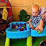 Asher joined the competition — help win amazing prizes! toddler, child, toy, building_blocks, play_table, indoor, playroom, tent, race_car_tent, green_chair, wooden_wall, car_toy, colorful, floor_mat, casual_clothing, shorts, checkered_shirt, sitting, focused, playtime