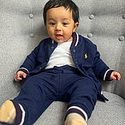 Kabir joined the competition — help win amazing prizes! toddler, child, baby, person, face, clothing, navy_blue, jacket, pants, socks, chair, upholstery, gray, indoor, portrait, cute, expression, seated, comfortable, young