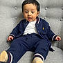 toddler, child, baby, person, face, clothing, navy_blue, jacket, pants, socks, chair, upholstery, gray, indoor, portrait, cute, expression, seated, comfortable, young