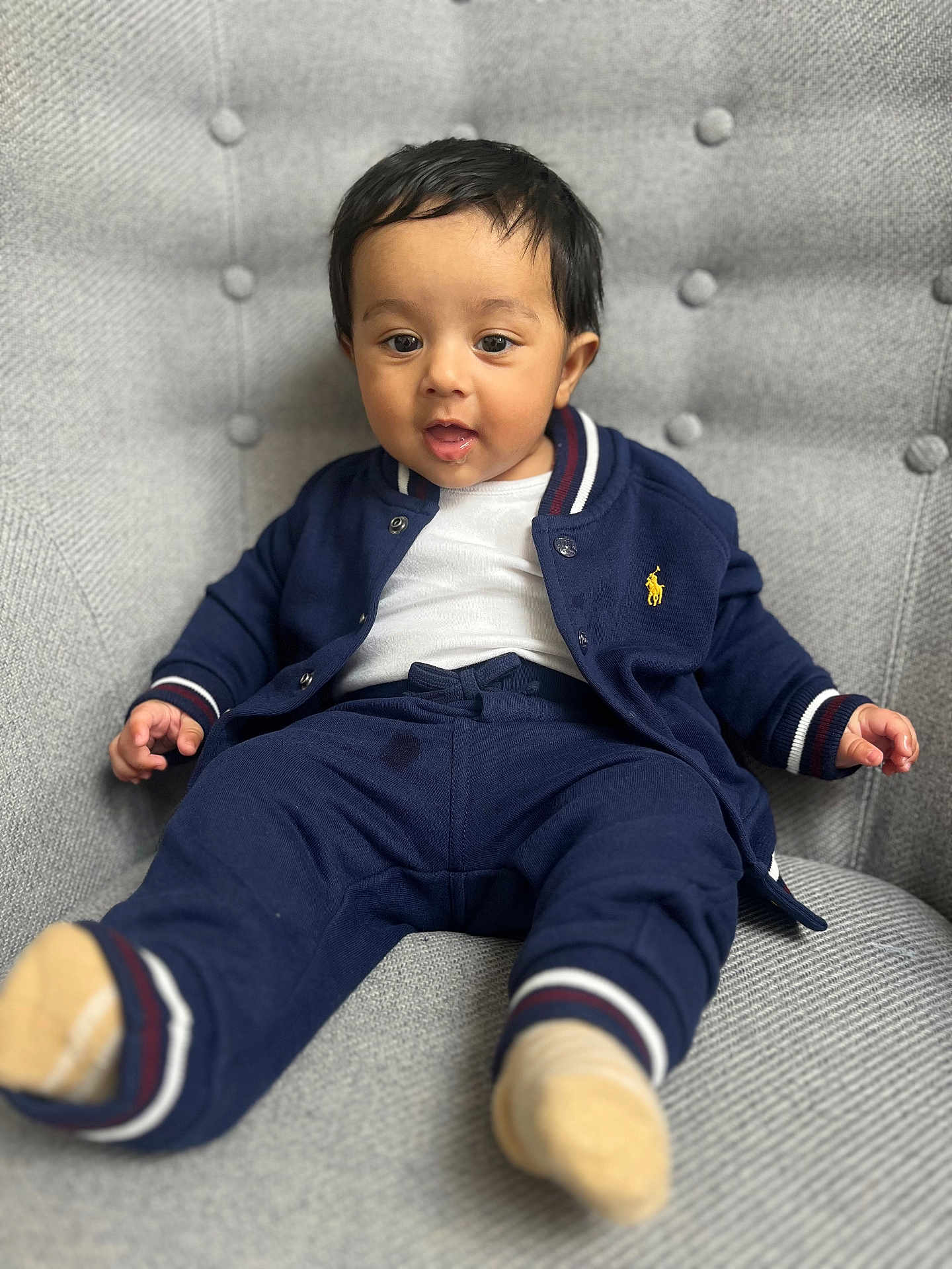 Kabir joined the competition — help win amazing prizes! toddler, child, baby, person, face, clothing, navy_blue, jacket, pants, socks, chair, upholstery, gray, indoor, portrait, cute, expression, seated, comfortable, young