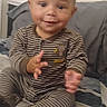 Ezra is registered to the contest to win money with this photo: baby, bed, blanket, child, couch, cute, feet, hand_gesture, happy, home, indoors, infant, legs, long_sleeves, pajamas, photography, portrait, sitting, smiling, striped_clothing