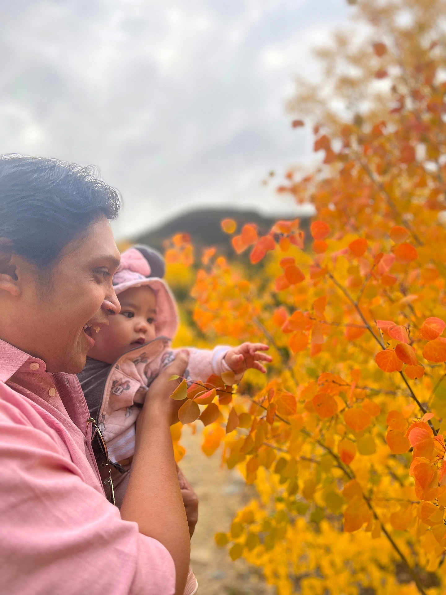 Cabrine is registered to the contest to win money with this photo: adult, baby, child, holding, autumn, leaves, orange, yellow, outdoor, nature, tree, hoodie, curious, smiling, portrait, side_view, fall, season, person, happy