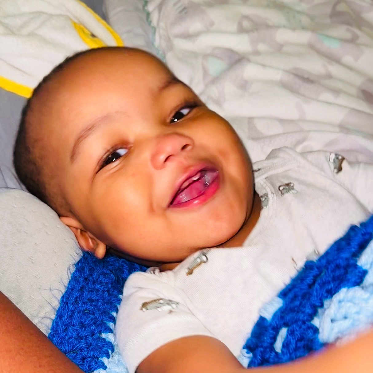 Imran joined the competition — help win amazing prizes! baby, smiling, blanket, blue, crochet, bed, bedding, infant, child, face, happy, person, portrait, sleepwear, lying_down, cuddly, cute, indoors, toddler, relaxed