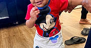 Imran is registered to the contest to win money with this photo: baby, carpet, child, clothing, cute, floor, footwear, furniture, hand_holding, happy, indoor, living_room, mickey_mouse, person, smile, sneakers, standing, support, television, toddler