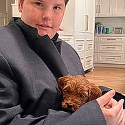 Rosie is registered to the contest to win money with this photo: person, puppy, dog, indoor, kitchen, oversized_clothing, brown_dog, holding, cute, pet, home, cabinets, floor, buttons, face, short_hair, cozy, casual, sleeves, wooden_floor