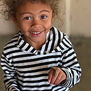 Nala joined the competition — help win amazing prizes! child, smiling, curly_hair, striped_hoodie, caterpillar, hand, face, portrait, indoor, happy, young, person, casual_clothing, closeup, cute, curiosity, natural_light, skin, eye, finger