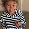 child, smiling, curly_hair, striped_hoodie, caterpillar, hand, face, portrait, indoor, happy, young, person, casual_clothing, closeup, cute, curiosity, natural_light, skin, eye, finger