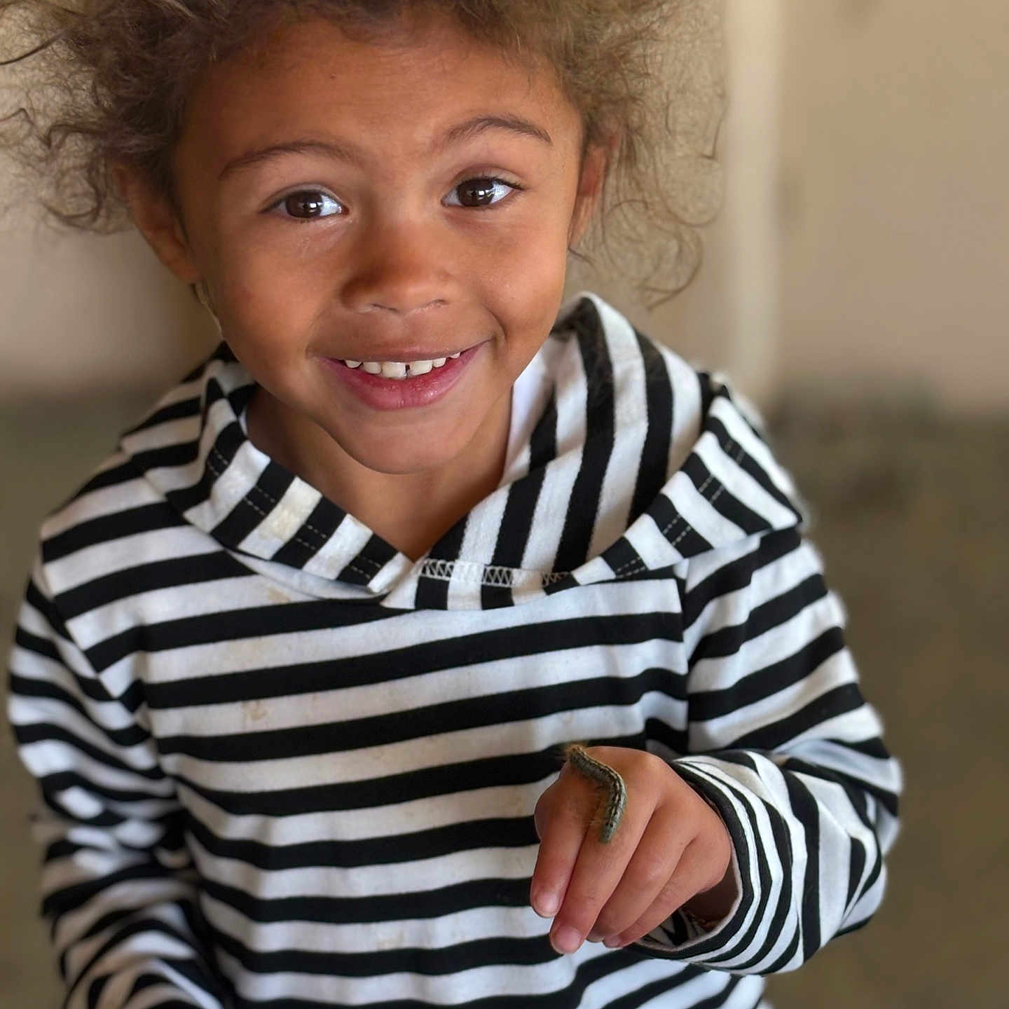Nala joined the competition — help win amazing prizes! child, smiling, curly_hair, striped_hoodie, caterpillar, hand, face, portrait, indoor, happy, young, person, casual_clothing, closeup, cute, curiosity, natural_light, skin, eye, finger