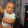 baby, bedroom, cartoon_shirt, child, cute, eyes, face, family, hair_buns, held, home, indoor, infant, person, portrait, sitting, smiling, striped_clothing, television, top_knots
