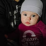 baby, child, beanie, clothing, face, blue_eyes, glossy_lips, portrait, indoor, person, hoodie, dark_background, close_up, cute, infant, apparel, text_on_clothing, rainbow, looking_at_camera, soft_lighting