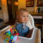 Iylee joined the competition — help win amazing prizes! baby, high_chair, toy, indoor, child, blue_eyes, denim_dress, curly_hair, table, wall_art, wooden_frame, lighting, furniture, person, portrait, cute, infant, room, decor, play