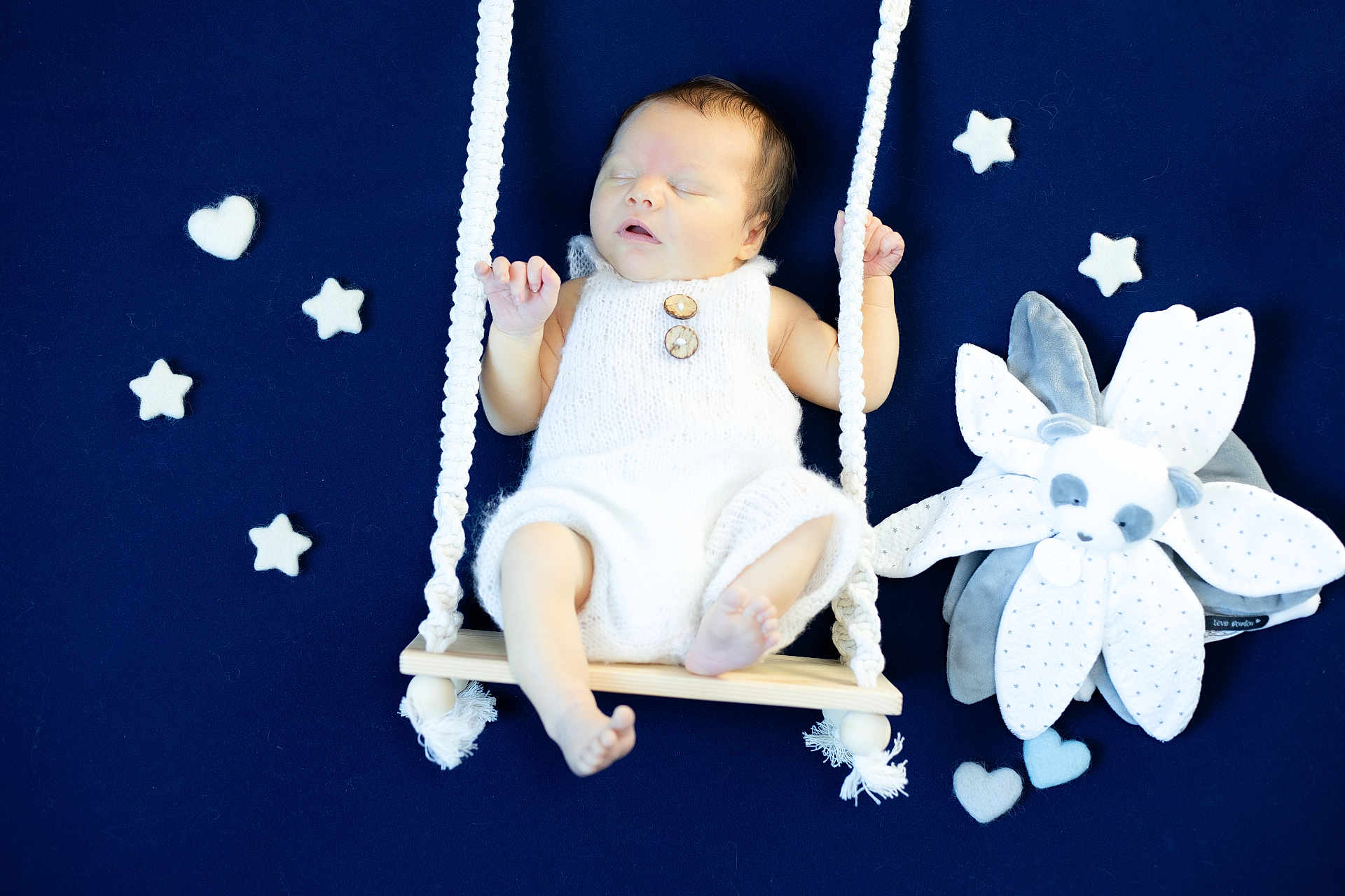 Oscar a rejoint le concours — aidez-le/la à gagner de superbes lots ! baby, sleeping, swing, white_clothing, knitwear, wooden_swing, soft_toy, plush, felt_stars, felt_hearts, blue_background, infant, peaceful, cute, child, portrait, indoors, newborn, hand_knit, toy_flower