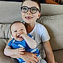 Arthur participe au concours pour gagner de l'argent avec cette photo : baby, child, sibling, glasses, smile, couch, indoor, happy, holding, blue_clothing, striped_pants, white_shirt, cute, family, portrait, furniture, infant, young_child, home, person