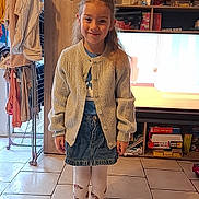 Liana a rejoint le concours — aidez-le/la à gagner de superbes lots ! cardigan, casual_clothing, child, clothes_rack, denim_skirt, footwear, furniture, girl, hair, happy, home, indoor, living_room, person, shoes, smiling, standing, television, tights, tile_floor