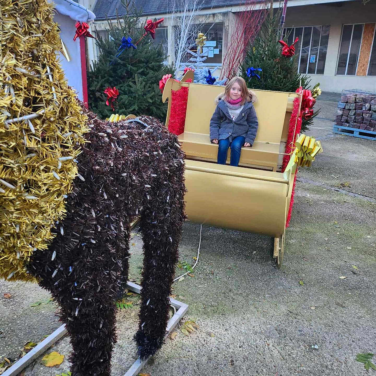 Liana participe au concours pour gagner de l'argent avec cette photo : bench, building, child, christmas_decorations, cold_weather, concrete, decoration, festive, holiday, holiday_spirit, outdoor, person, reindeer, ribbons, seasonal, sleigh, smiling, tinsel, tree, winter_clothing