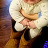 Eric is registered to the contest to win money with this photo: baby, child, boots, brown_boots, floor, wooden_floor, indoor, person, smiling, cute, holding, clothing, face, happy, adult, glasses, sitting, playful, text_overlay, blue_text
