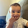 Bradley is registered to the contest to win money with this photo: baby, child, smiling, fingers, onesie, clothing, indoor, couch, comfortable, cute, face, happy, person, infant, portrait, young_child, snuggly, hand, eyes, sitting