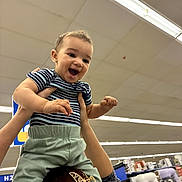 Bradley joined the competition — help win amazing prizes! child, toddler, smiling, happy, person, hands, indoor, store, shopping, appliances, fluorescent_lighting, ceiling, clothing, striped_shirt, green_pants, hair_accessory, lifting, joy, playful, retail