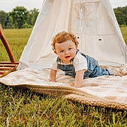 Walker is registered to the contest to win money with this photo: baby, toddler, infant, curly_hair, denim_overalls, blanket, teepee, balloons, grass, field, outdoor, portrait, crawling, smile, blue_eyes, picnic, playful, sunlight, nature, family